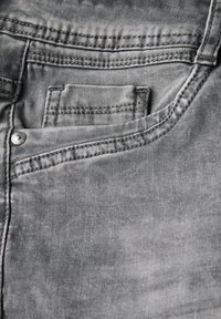 Grijze denimstof met zakken, zichtbare stiksels en een glanzende zilveren klinknagel. Zachte textuur met een licht versleten uiterlijk.