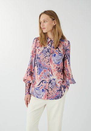 Blouse florale multicolore avec un mélange de teintes roses et violettes, un devant à boutons et des manches amples en tissu léger.