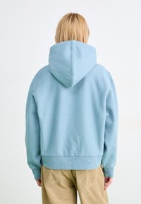 Felpa con cappuccio blu chiaro, realizzata in tessuto morbido, con una vestibilità comoda e polsini a costine. Design casual con orlo dritto e dettagli minimi.