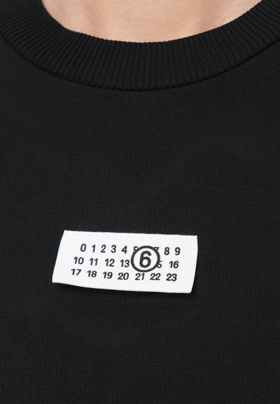 Black sweater with a ribbed crew neckline, featuring a white label with a size '6' and numbered grid printed in black.