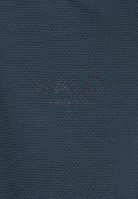 Mørkeblå tekstureret stof med svag "HALO"-tekst og mindre ulæselig tekst nedenunder i midten.