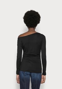 Sort langærmet top med asymmetrisk udskæring, glat stof, rynket detalje ved taljen og parret med blå denim.