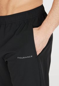 Zwarte sportshorts van lichtgewicht stof, met een elastische tailleband, zijzakken en een reflecterend "ENDURANCE" logo.