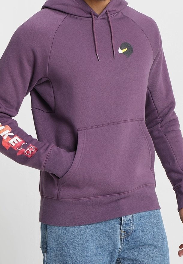 Fialová mikina s kapucí a přední kapsou, bílé logo Nike na prsou a červený nápis "NIKE SB" na rukávu. Měkký materiál, uvolněný střih.