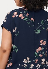 Navy floral blouse featuring short sleeves, a relaxed fit, and a pattern of light pink and green flowers on a textured fabric.