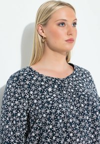 Marinefarbener Langarmshirt mit weißen Schneeflockenmuster und subtilen Farbakzenten. Rundhalsausschnitt, weicher Stoff mit glatter Textur.