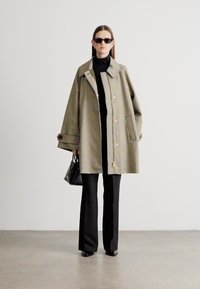 Manteau oversize à carreaux beige et noir, avec un large col, de gros boutons et des poches latérales, associé à un pantalon noir slim et un sac à main.