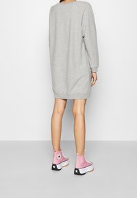 Sweat-shirt gris à manches longues avec poignets côtelés, associé à des baskets montantes roses avec des accents noirs et blancs.