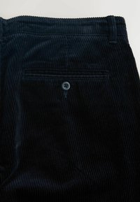 Pantalon en velours côtelé bleu marine avec texture côtelée verticale, une poche arrière avec un bouton noir et des passants de ceinture à la taille.