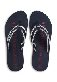 Τα σκούρα μπλε λαστιχένια σαγιονάρες διαθέτουν λουράκια με κατά μήκος ρίγες λευκού και κόκκινου χρώματος, με την επιγραφή "TOMMY HILFIGER" σε κόκκινο στην σόλα. Απαλή υφή, casual σχεδιασμός.