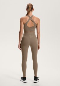 Hnedý športový crop top s dizajnom kríženia na chrbte a výrezom v tvare kľúča, doplnený o zodpovedajúce legíny s vysokým pásom a chevronovými švami.