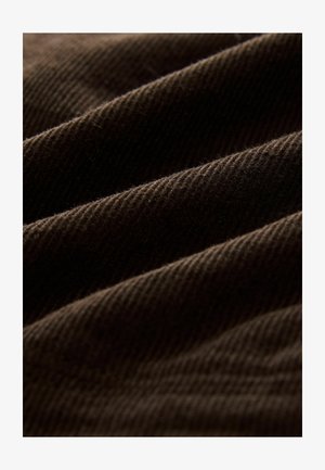 Dunkelbrauner Cordstoff mit ausgeprägter Rippstruktur. Die Falten verleihen Tiefe und zeigen die weiche, plüschige Qualität des Materials.