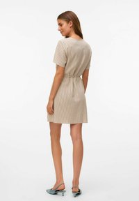 Abito beige corto con strisce verticali, maniche corte e una cintura aderente in vita. La modella indossa sandali blu con tacco basso. Tessuto di trama liscia.