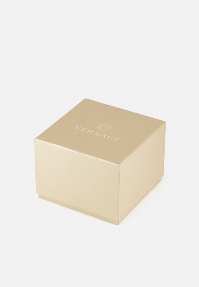 Zelta taisnstūra kaste ar teksturētu virsmu, kuras augšpusē ir iepresēts "VERSACE" logo gaišākā tonī.