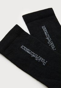 Svarta strumpor med ribbad textur; har ljusgrå texten "ParkPerformante" på sidorna. Enkel design i rörformad stil.