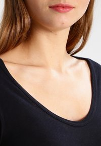 Maglietta nera con scollatura profonda, tessuto morbido e texture liscia. Dettagli limitati visibili fino alla clavicola.