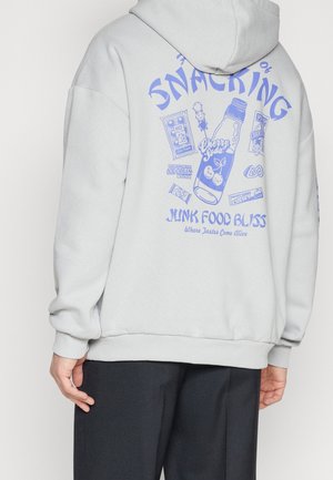 Sudadera gris claro con una textura suave, que presenta un estampado gráfico azul de aperitivos y bebidas en la parte posterior. Puños y dobladillo acanalados.