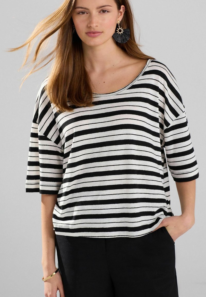Haut rayé noir et blanc avec un large décolleté et des manches 3/4, fabriqué en tissu doux, associé à un pantalon sombre.