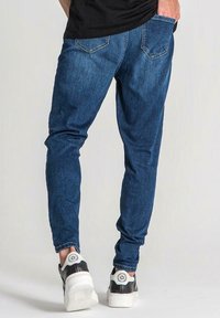 Niebieskie jeansy z denimu o dopasowanym kroju, z dwoma tylnymi kieszeniami i zwężanymi nogawkami, zestawione z czarno-białymi tenisówkami.