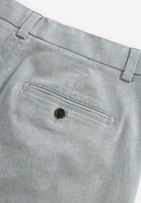 Pantalons gris clair avec un tissage texturé, dotés d'une poche arrière avec un système de fermeture à bouton sombre et des détails de taille plate.