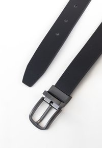 Cinturón de cuero negro con acabado mate, hebilla rectangular de metal plateado y varios orificios de ajuste; forma plana con extremo afilado.