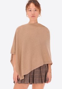 Poncho beige realizzato in morbido tessuto, caratterizzato da un design asimmetrico e svasato con maniche corte. È noto per la sua superficie liscia e lo stile minimalista.