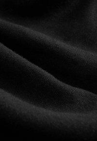 Gros plan d'un tissu noir doux avec une texture fine et des plis légers créant des vagues lisses dans le matériau.