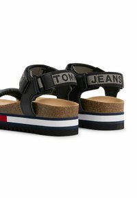 Sandali neri con larghe cinghie che presentano il testo "TOMMY JEANS", suola in sughero e suola a strisce multi-colorate. Chiusura con fibbia regolabile.