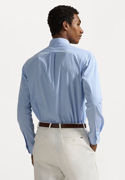 Lichtblauwe gestreepte overhemd met lange mouwen, een button-down kraag en enkele manchetten, gedragen met crèmekleurige broek en een bruin leren riem. Effen stoftextuur.