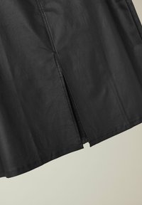 Zwarte neplederen rok met een rechte snit, voorzien van een kleine split aan de zoom en een gladde textuur. Duurzame stiksels langs de randen.