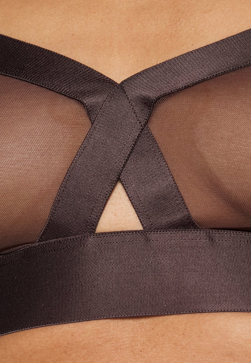 Sostenedor marrón con paneles de malla y una banda ancha. Presenta un diseño en forma de cruz en las correas, proporcionando un acento geométrico. Textura suave.