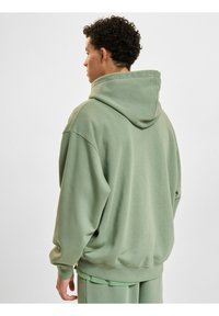 Sweat à capuche vert avec une coupe décontractée, grande capuche et poignets côtelés. Texture de tissu douce, design uni sans motifs ni accents.