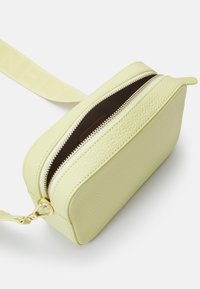 Borsa a tracolla gialla in pelle, con forma rettangolare, superficie testurizzata, zip dorata e una tracolla piatta. Interno di colore marrone scuro.