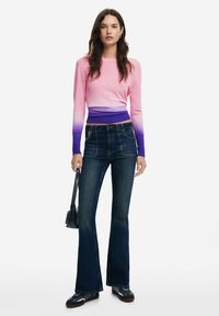 Pikkade varrukatega tipp, millel on roosa kuni lilla gradient, koos tumeda pesuga laiadest teksadest. Mudel hoiab käes väikest musta käekotti.