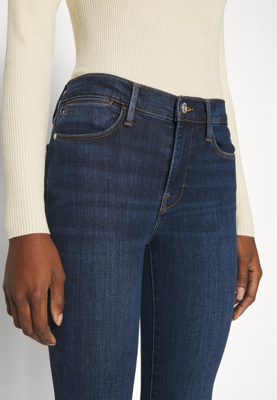 Jeans slim fit bleu foncé avec une taille mi-haute, des coutures contrastées et un design classique à cinq poches. Texture en denim brossé.