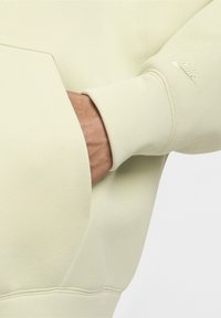 Svetlozelen sweatshirt Nike z teksturirano površino, ki ima sprednjo žep in vezeno logo na rokavu. Preprost in minimalističen dizajn.