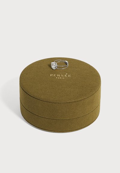Caja de joyas redonda de ante verde oliva con texto dorado "PERSÉE PARIS", rematada con un anillo de plata con una gran piedra preciosa clara.