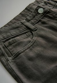 Dunkelgraue Jeans, schräg präsentiert, mit einer Vordertasche, Knopfverschluss und kontrastierenden Nähten auf dem Stoff.