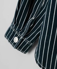 Puño de camisa a rayas hecho de tela azul oscuro con rayas verticales blancas, con un botón a presión plateado y un detalle de costura visible.