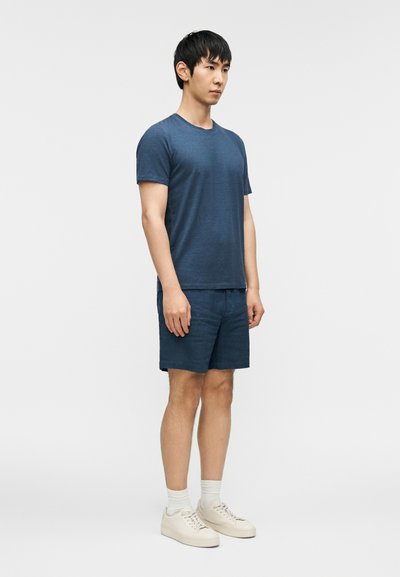 Μπλε ναυτικό μπλουζάκι με στρογγυλή λαιμόκοψη από απαλό ύφασμα, συνδυασμένο με σορτς ταιριαστού χρώματος, φορεμένο με λευκά αθλητικά παπούτσια και κάλτσες. Απλός, καθημερινός σχεδιασμός.