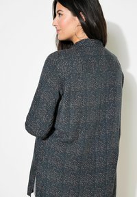 Dunkelblaue Bluse mit kleinen, mehrfarbigen Punkten. Sie hat einen Knopfverschluss im Rücken, lange Ärmel und eine lockere Passform mit seitlichen Schlitzen.