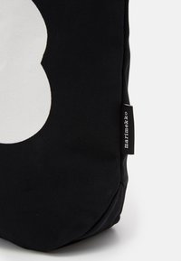 Black canvas bag featuring a large white flower shape. Includes a small label on the side with "marimekko" text. Textured material.