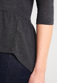 Dunkelgraues Peplum-Top aus weichem Strickstoff, mit gerafftem Bund und Dreiviertelärmeln, kombiniert mit dunkler Denim.