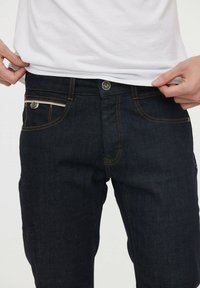 Jeans de mezclilla oscura con un diseño ajustado, que presentan costuras naranjas, bolsillos frontales y un cierre de botón metálico.