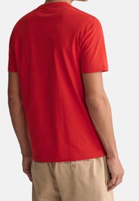 Rotes Baumwoll-T-Shirt mit Rundhalsausschnitt und kurzen Ärmeln, das eine glatte Textur aufweist. Das Shirt wird mit hellen Shorts kombiniert.