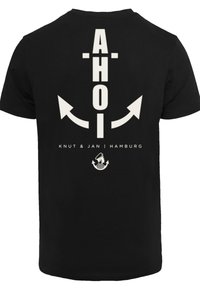 Zwarte T-shirt met grote witte "AHOI" tekst, twee pijlen ontwerpen en kleinere tekst "Knut & Jan | Hamburg" met daaronder een anker grafiek.