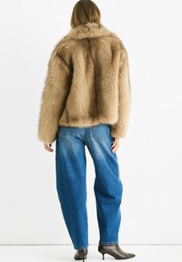 Brown faux fur jacket with a boxy fit and wide sleeves, paired with loose blue denim jeans and dark heeled shoes.