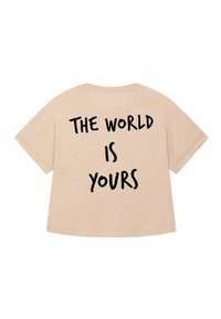 T-shirt en coton beige à manches courtes et coupe ample. Texte imprimé en noir gras au dos : « LE MONDE EST À VOUS. »