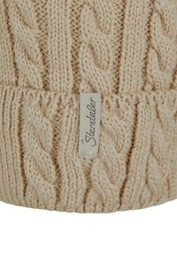 Beige gestrickte Mütze mit einem Kabelmuster, die eine weiche Textur aufweist und an der Kante ein sichtbares Markenetikett hat.