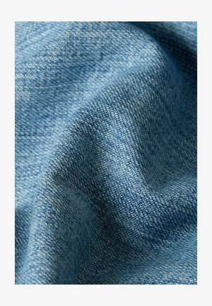 Close-up of light blue woven fabric with visible texture and soft folds creating gentle shadows.